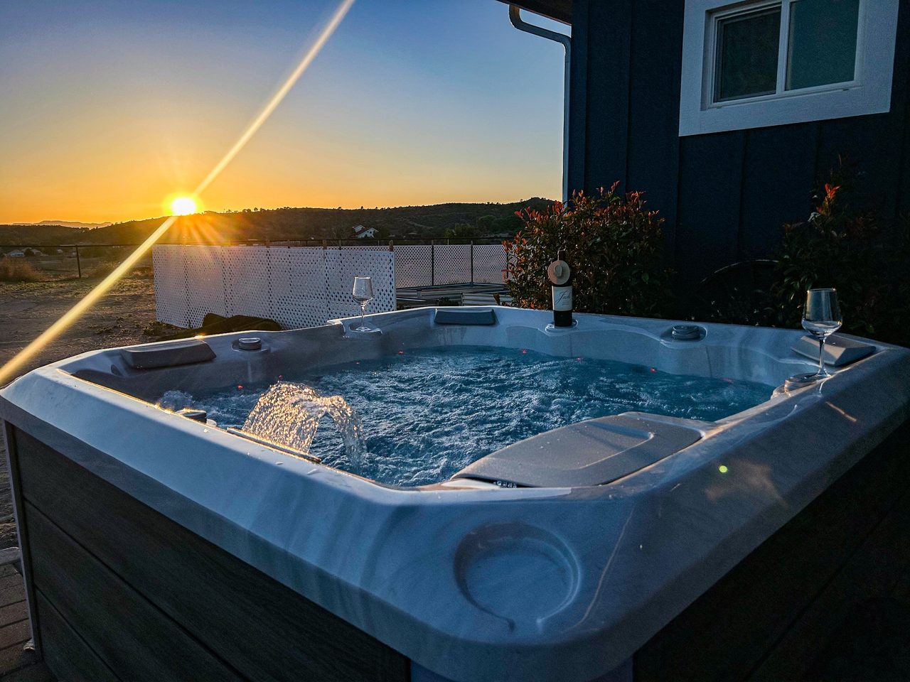 Bubbling hot tub on a deck beside the house as the sun sets over the hills