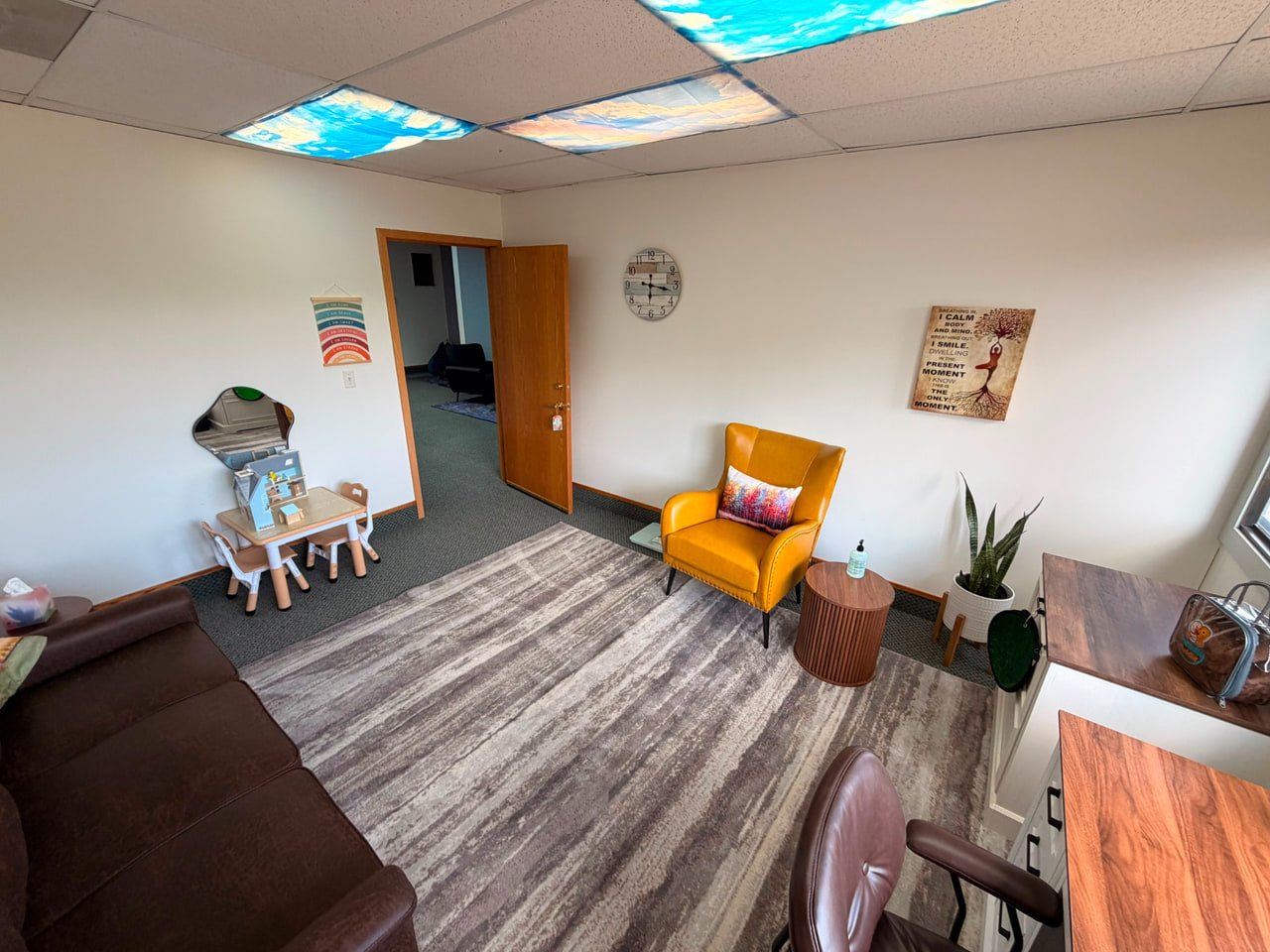 Therapy room with a yellow armchair, small children's table, plants and a striped rug